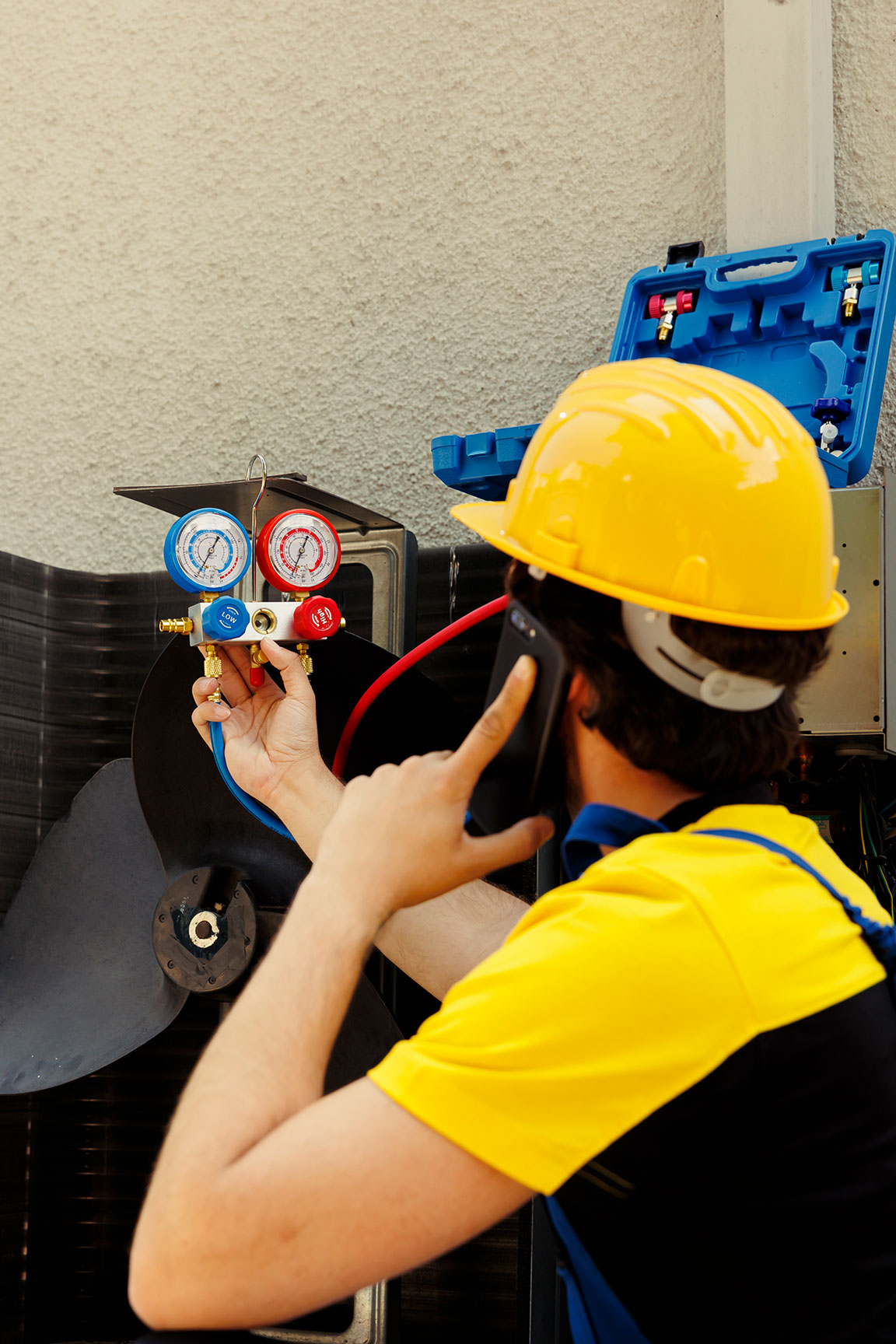 Technician in yellow helmet adjusts HVAC gauges during maintenance.